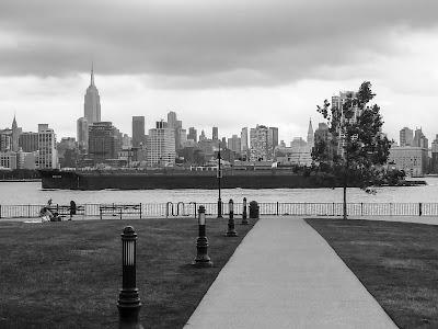 Black barge carrying  red containers going up river, passing the Empire State Building