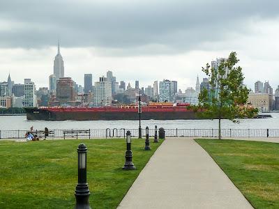 Black barge carrying  red containers going up river, passing the Empire State Building