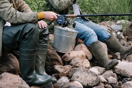 Men sitting on the rocks holding a baitcasting reel with silver bucket