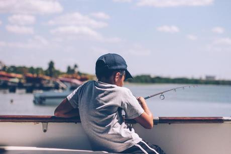 A boy wearing a black hat fishing on a boat using boat rods