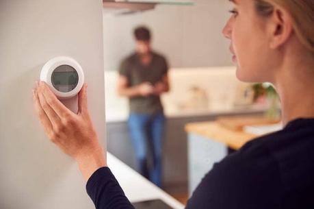 Close up image of woman adjusting a wall mounted digital central heating thermostat control