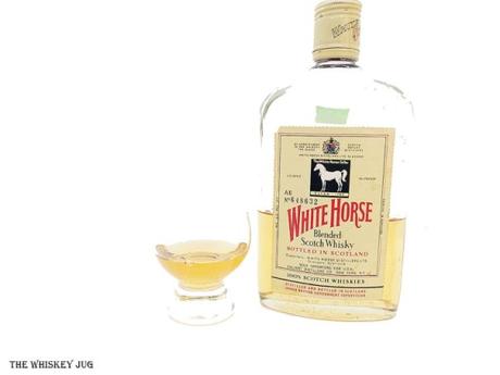 White background tasting shot with the 1970s White Horse Blended Scotch bottle and a glass of whiskey next to it.