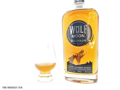 White background tasting shot with the Wolf Moon Bourbon bottle and a glass of whiskey next to it.