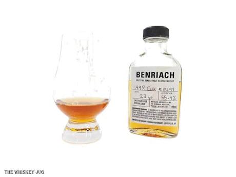 White background tasting shot with the BenRiach 23 Years - 1998 Cask 10297 sample bottle and a glass of whiskey next to it.