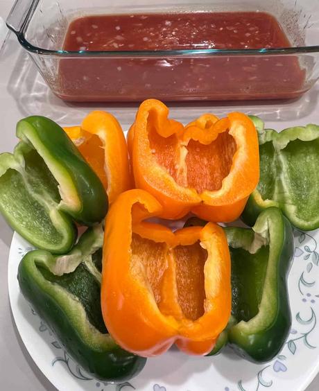 Bell peppers ready to be stuffed and a casserole dish filled with sauce