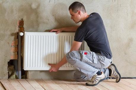 Professional plumber installing radiator on wall