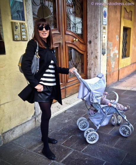 A real Italian mom looking stylish in a striped Zara top, plather shorts in black, reminiscence rings Marc by Marc Jacobs bag Ukita pushing a stroller in Modena Italy Emilia Romagna.  Wearing sunglasses.