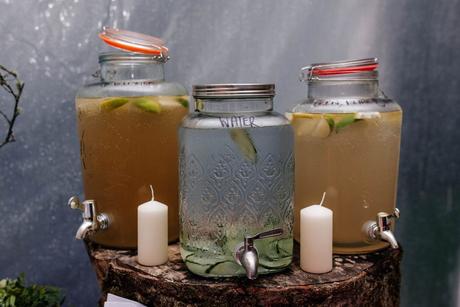At a summer wedding, a refreshing and colorful array of non-alcoholic drinks are served in mason jars. The drinks are garnished with fresh fruit and herbs, adding a touch of elegance and sweetness to the celebration. The jars are set up on a rustic wooden table with a floral arrangement in the background, creating a charming and picturesque scene. The drinks are perfect for guests who want to stay cool and hydrated while enjoying the festivities.
