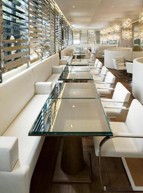 Simone Design Blog|Commercial interiors that are inspiring with its color scheme|Restaurant is decorated in white and gold. The glass table tops and pendant lighting complements the modern look of the room.