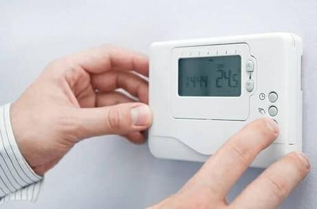hands adjusting a thermostat on a wall