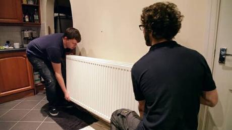 two men lifting a radiator from its mounting on a wall