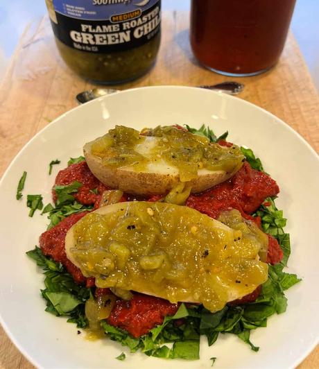 a potato covered with green Chile sitting on top of a bed of salad greens and New Mexican red Chile sauce