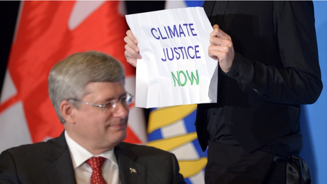 A protestor holds a sign during an event with Prime Minister Stephen Harper at the Vancouver Board of Trade on Monday Jan. 6, 2013. (Jonathan Hayward / THE CANADIAN PRESS)