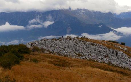Hiker on a rocky outcrop with the Julian Alps in the background.