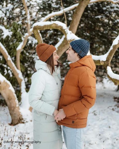 winter engagement photos couple in a snowy forest by a tree