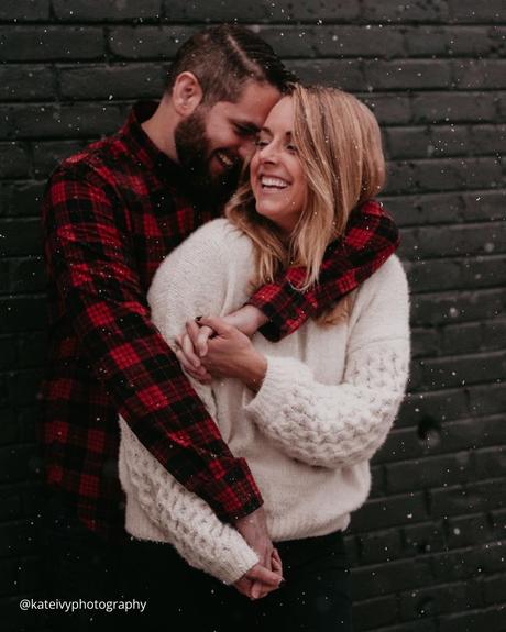 winter engagement photos couple is hugging under falling snow