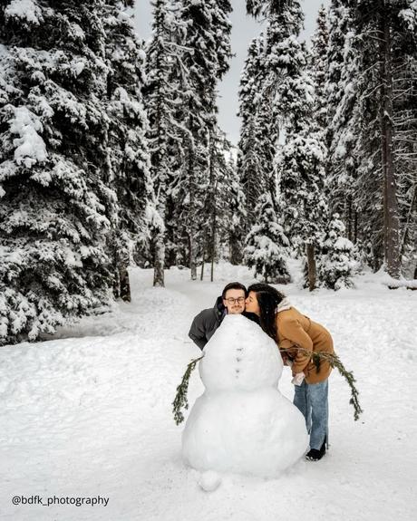 winter engagement photos girl is kissing boy near snowman