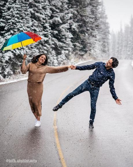 winter engagement photos girl with umbrella is shooting with funny guy under the snow