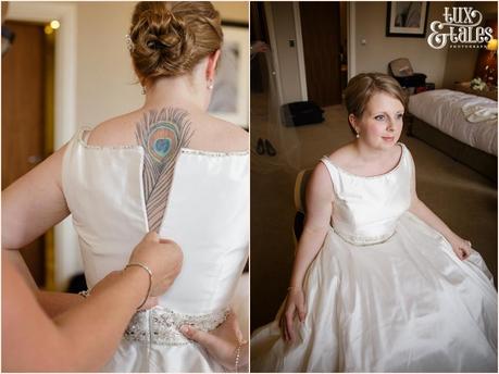 Bride with peackcock feather tattoo down her back is zipped into her wedding dress at York wedding in Cedar Court Grand Hotel