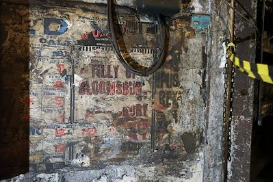 Photograph of dirt-stained, tattered theater posters. Fragments of the names of Shakespeare plays are visible, and the words 'Tilly of Bloomsbury' are large and legible in the center.