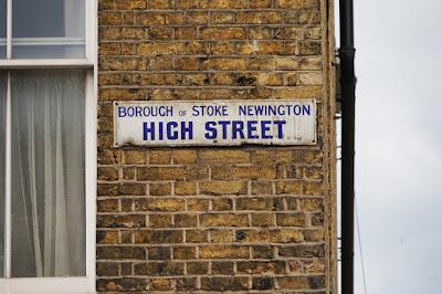 Photograph of a white, rectangular sign with royal blue letters saying 'BOROUGH OF STOKE NEWINGTON HIGH STREET'