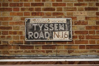 A sign for 'Tyssen Road' is a patchwork of different colours and texts - the borough and postcode details appear to have been stuck on later.