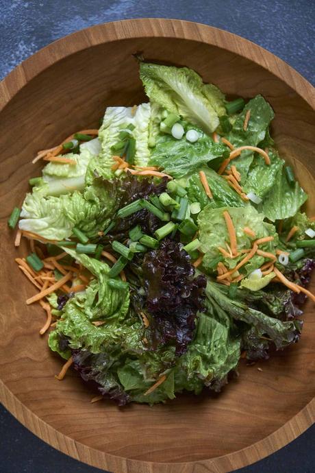 adding mixed greens into a salad bowl for korean lettuce salad