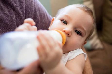 Mother lovingly holding her baby while feeding with a bottle in a warm, cozy home setting.