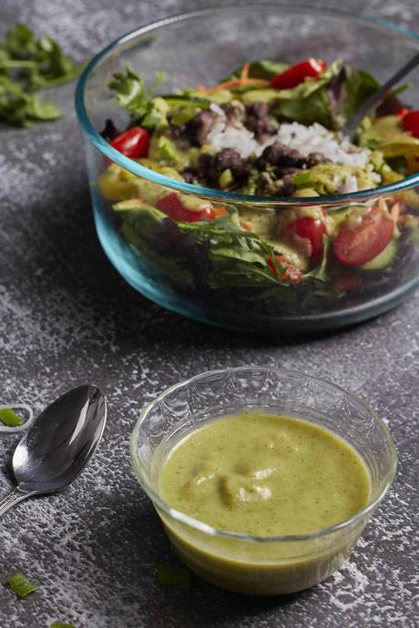 A dish of green chile lime salad dressing with a big salad in the background 