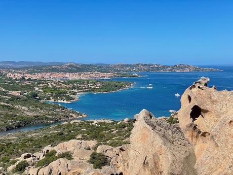 Hilltop view in the Maddalena Islands with rocky boulders in the foreground and a curving bay and turquoise waters beyond