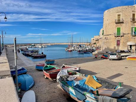 The quiet traditional fishing harbour of Giovinazzo with boats in the water and out on the shore and attractive stone buildings and blue skies