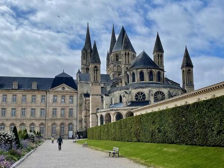 Exterior of Caen cathedral with turreted towers and ornamental hedges and a path leading up to a set of grand buildings