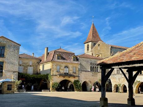 Central square of Monpazier in Dordogne with late afternoon shadow partially over the square and the medieval buildings bathed in a warm glow