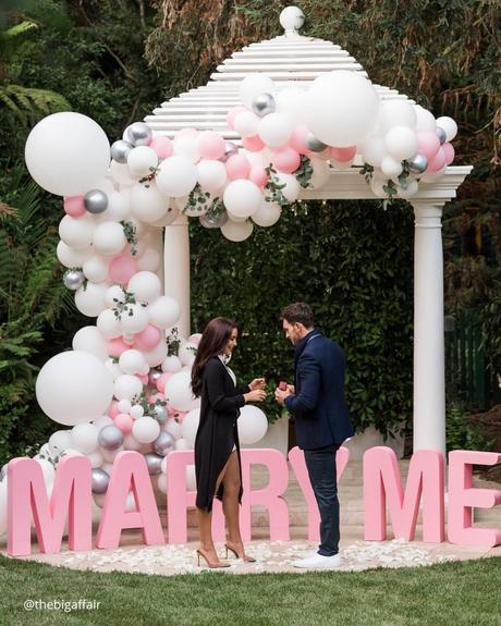 engagement photo captions the romantic picture of proposal arch with pink baloons and couple in the moment of proposal