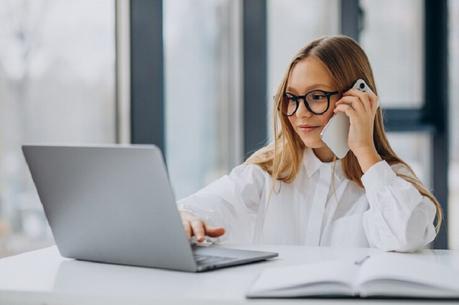 girl in white shirt using laptop talking phone