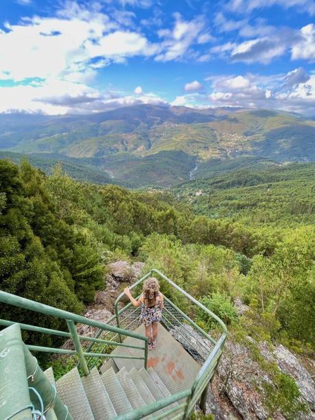 Woman standing on the steps of a viewing platform looking out over an expansive view of a green valley in northern portugal