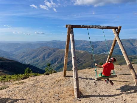 Alex Tiffany swinging on a swing on the summit of Serra de Sao Macario mountain in Portugal with blue skies and expansive views