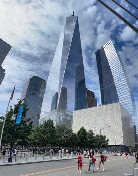 The gleaming One World Trade Center skyscraper with people crossing the road in the foreground