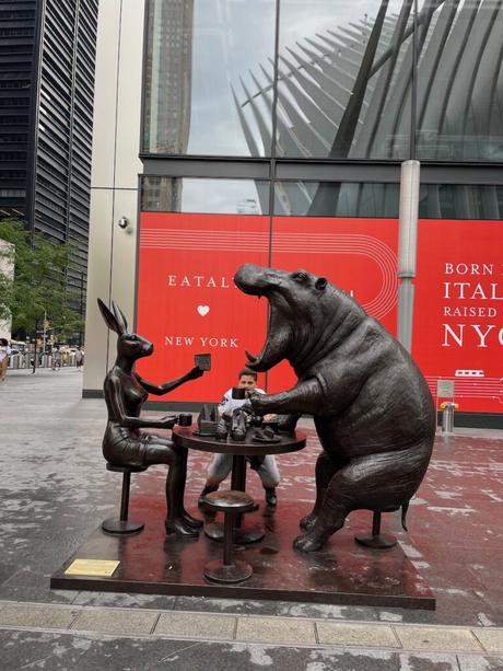 Bronze sculpture of a hippo and a hare sat opposite each other at a small table