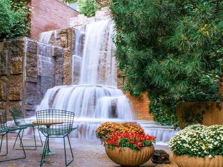 Waterfall inside Greenacre Park with ornamental flowers and a table with chairs