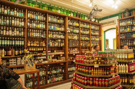 A quaint shop filled with shelves of colorful bottles, jars, and local products, with customers browsing the offerings.