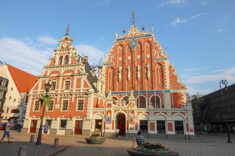 The ornate facade of the House of the Blackheads, a historic building in Riga, Latvia, characterized by its red brick exterior, white decorative elements, and several statues and intricate carvings adorning the top.