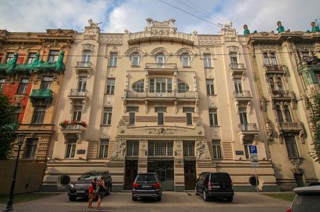 A richly ornamented residential building with classical and Baroque architectural elements, including sculptures and balconies. Two people stand near the entrance.