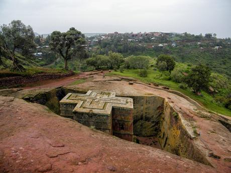 A rock-hewn church, showing its rectangular, windowed structure with weathered stone walls and a mossy appearance, surrounded by a carved-out trench.