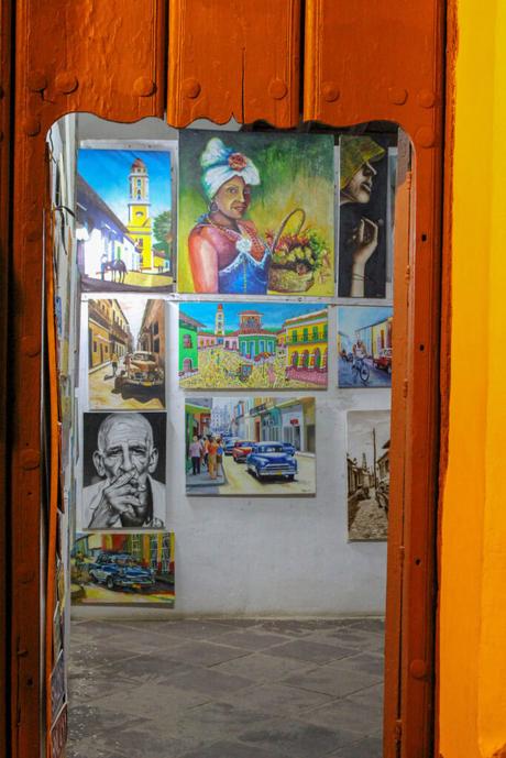 An open doorway leading to a small gallery filled with paintings depicting colorful scenes of Cuban life and culture.