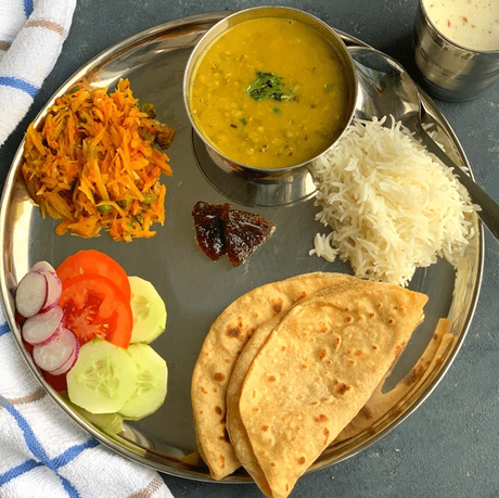 Indian food lunch thali with cucumber tomato onion salad chapati rice dal vegetables and pickle