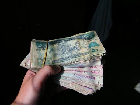 A hand holds a thick bundle of Somaliland currency notes, predominantly 500 Somaliland shilling bills, against a dark background.