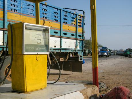 A brightly colored yellow and red fuel pump in front of a large, blue cargo truck at a roadside station in Somaliland.