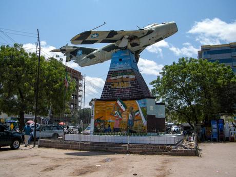 A monument in Hargeisa, Somaliland, displaying a decommissioned fighter jet mounted on a pedestal with murals depicting scenes from the struggle for independence.