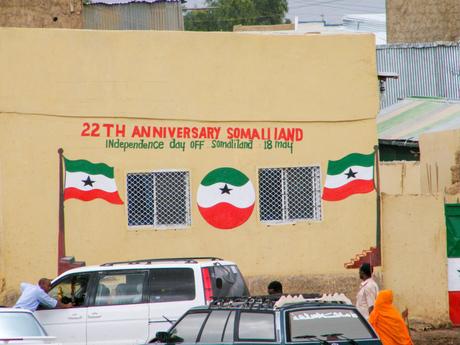 A mural painted on a yellow wall celebrating the 22nd Anniversary of Somaliland Independence on May 18th, with the Somaliland flag and people passing by below.